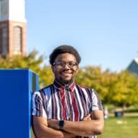 Man standing in grassy area with arms crossed, smiling